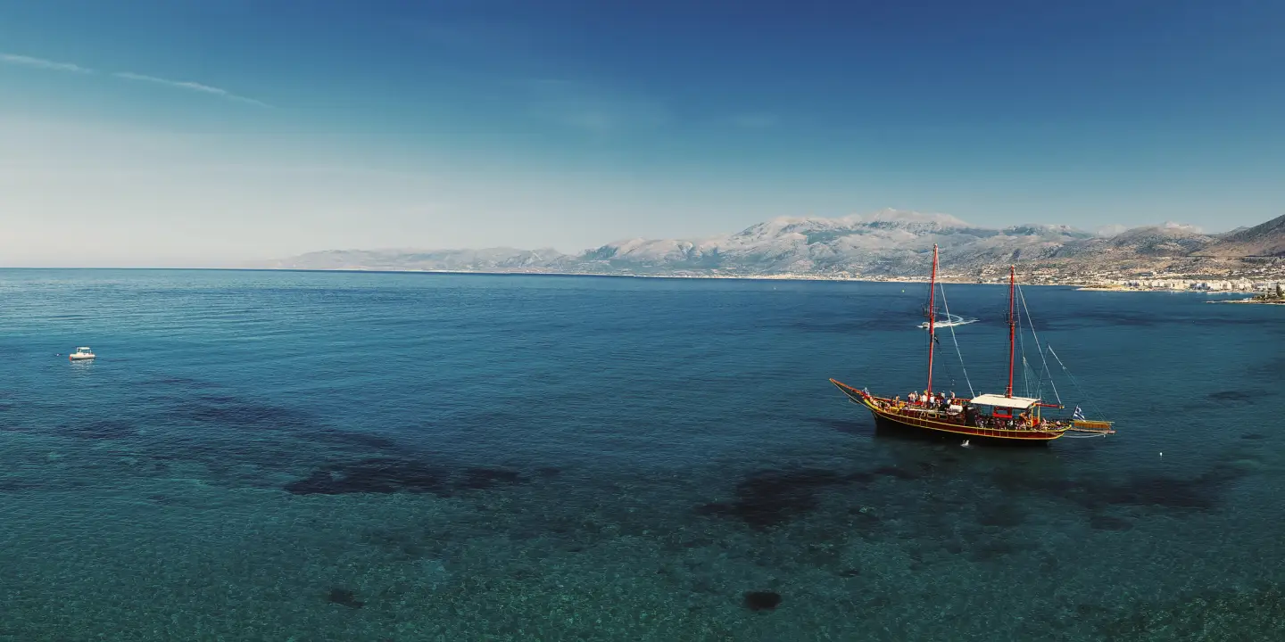 Beautiful scenery - traditional old fashioned cruise boat docked to the sand shore and colorful blue azure crystal clear water of Aegean Sea