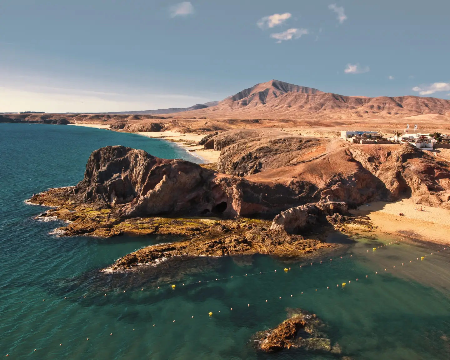 Blick auf die felsige Küste und die Papagayo-Strände auf Lanzarote mit türkisblauem Meer und karger Vulkanlandschaft im Hintergrund.