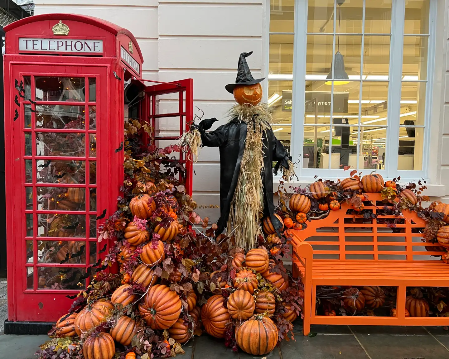 Rote Telefonzelle in London mit Kürbissen, Herbstdekoration und einer Halloween-Figur vor einem Geschäf