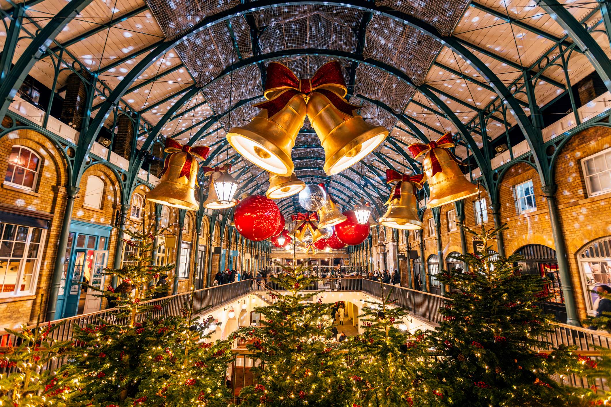 Festlich geschmückter Covent Garden in London mit beleuchteten Weihnachtsbäumen, großen goldenen Glocken und Weihnachtsdekoration.
