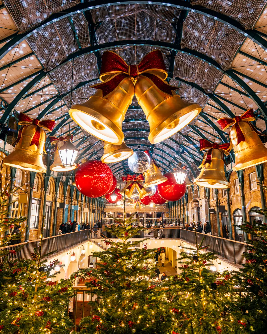 Festlich geschmückter Covent Garden in London mit beleuchteten Weihnachtsbäumen, großen goldenen Glocken und Weihnachtsdekoration.
