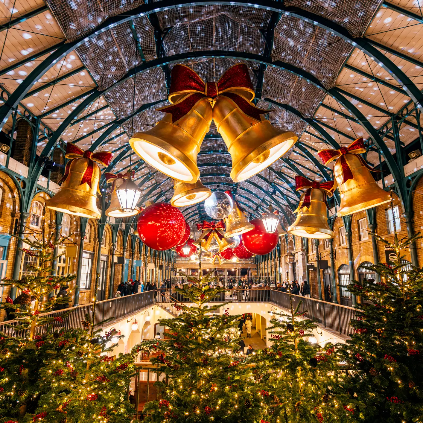 Festlich geschmückter Covent Garden in London mit beleuchteten Weihnachtsbäumen, großen goldenen Glocken und Weihnachtsdekoration.