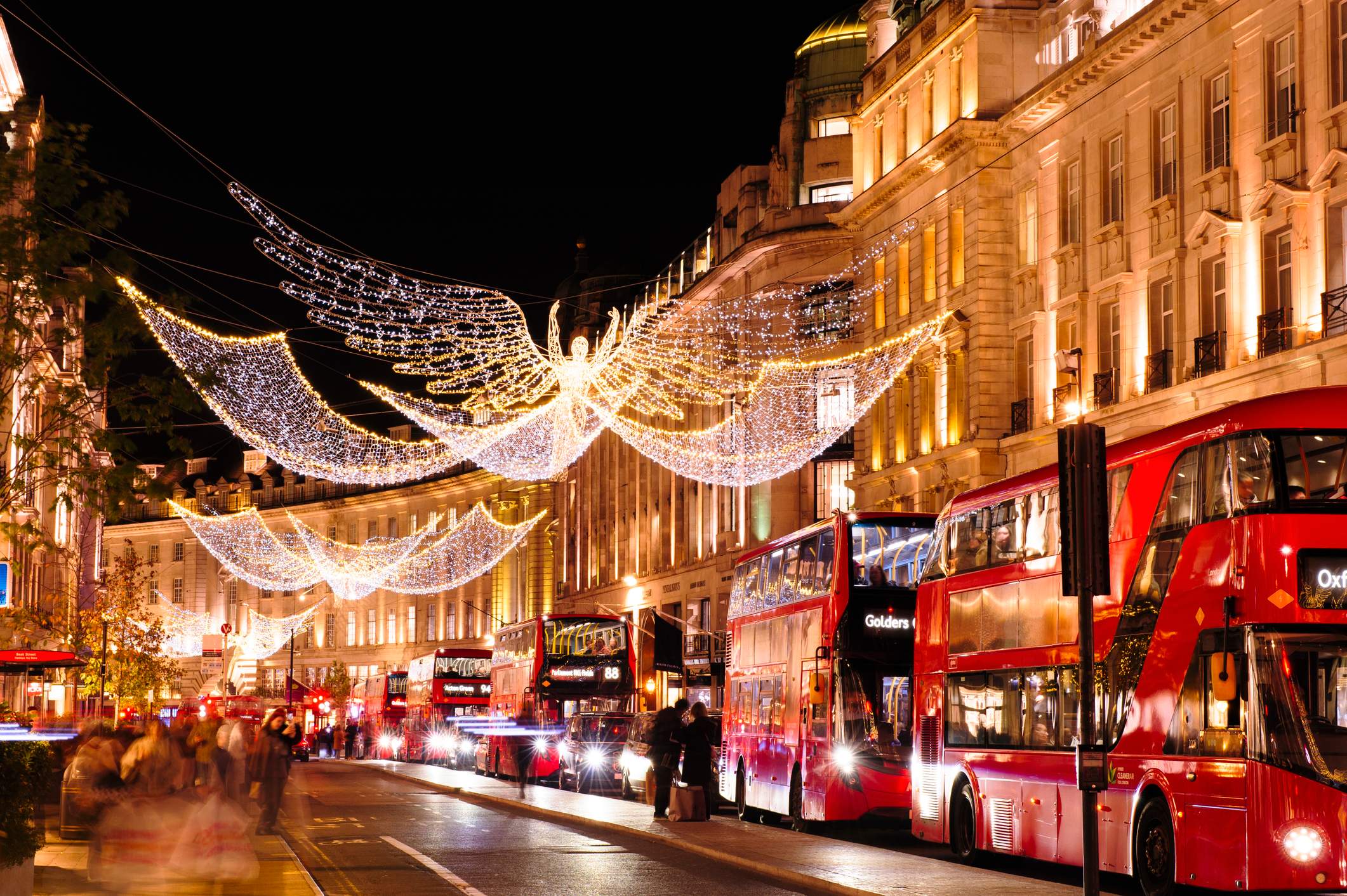 Weihnachtlich beleuchtete Regent Street in London mit leuchtenden Engelsfiguren und roten Doppeldeckerbussen.