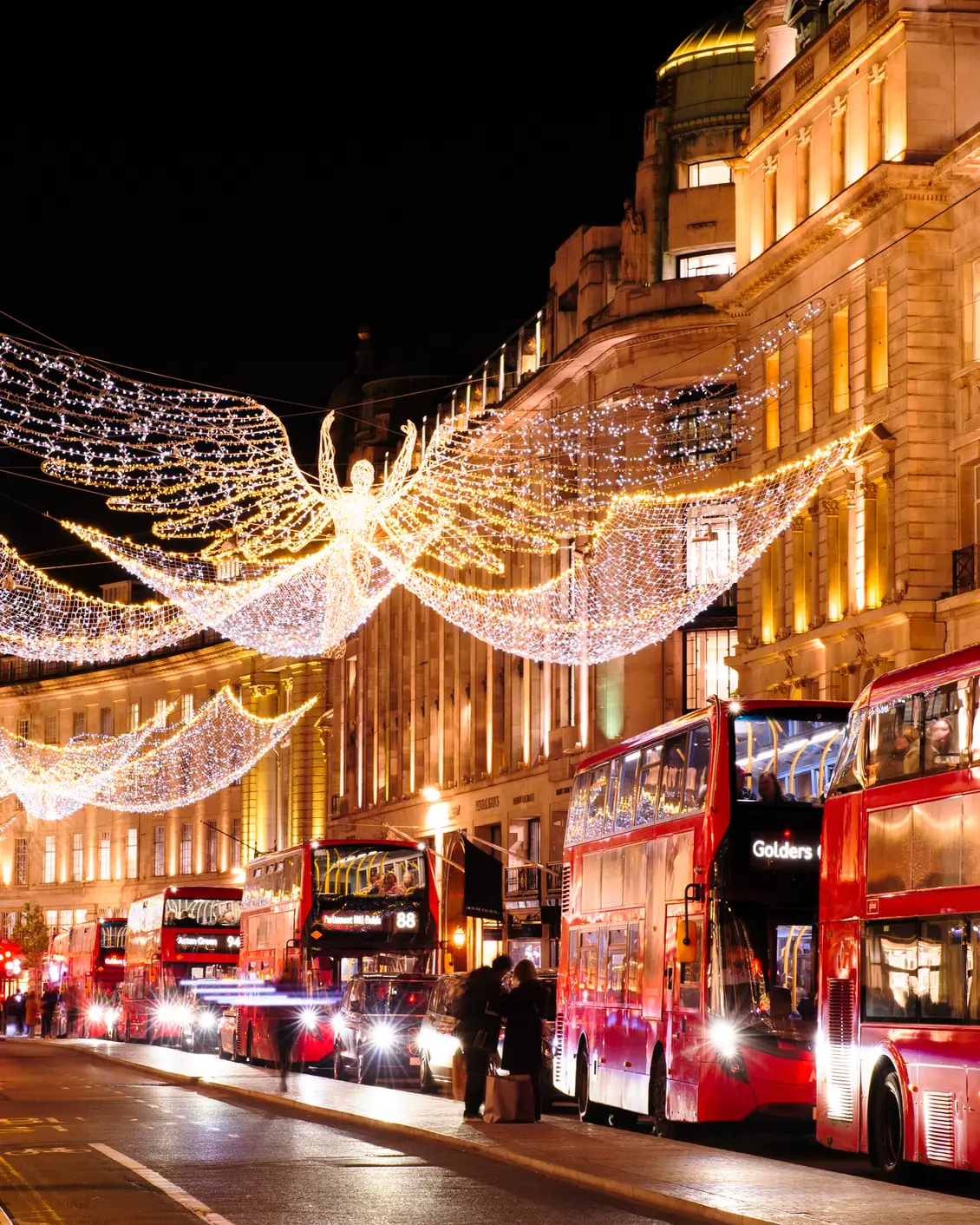 Weihnachtlich beleuchtete Regent Street in London mit leuchtenden Engelsfiguren und roten Doppeldeckerbussen.