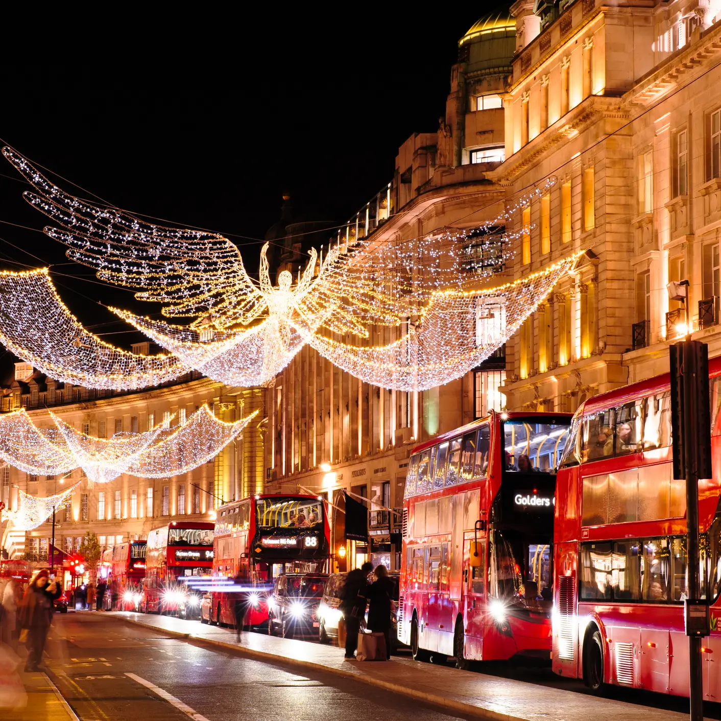 Weihnachtlich beleuchtete Regent Street in London mit leuchtenden Engelsfiguren und roten Doppeldeckerbussen.