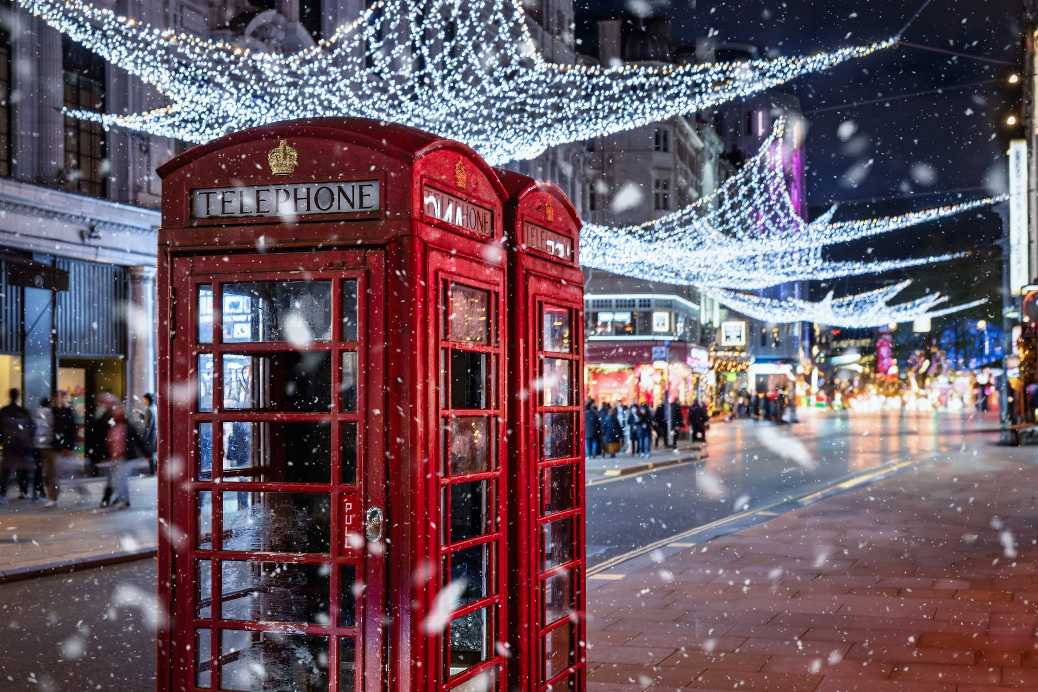 Rote Telefonzellen in London unter festlicher Weihnachtsbeleuchtung bei winterlichem Schneefall am Abend.