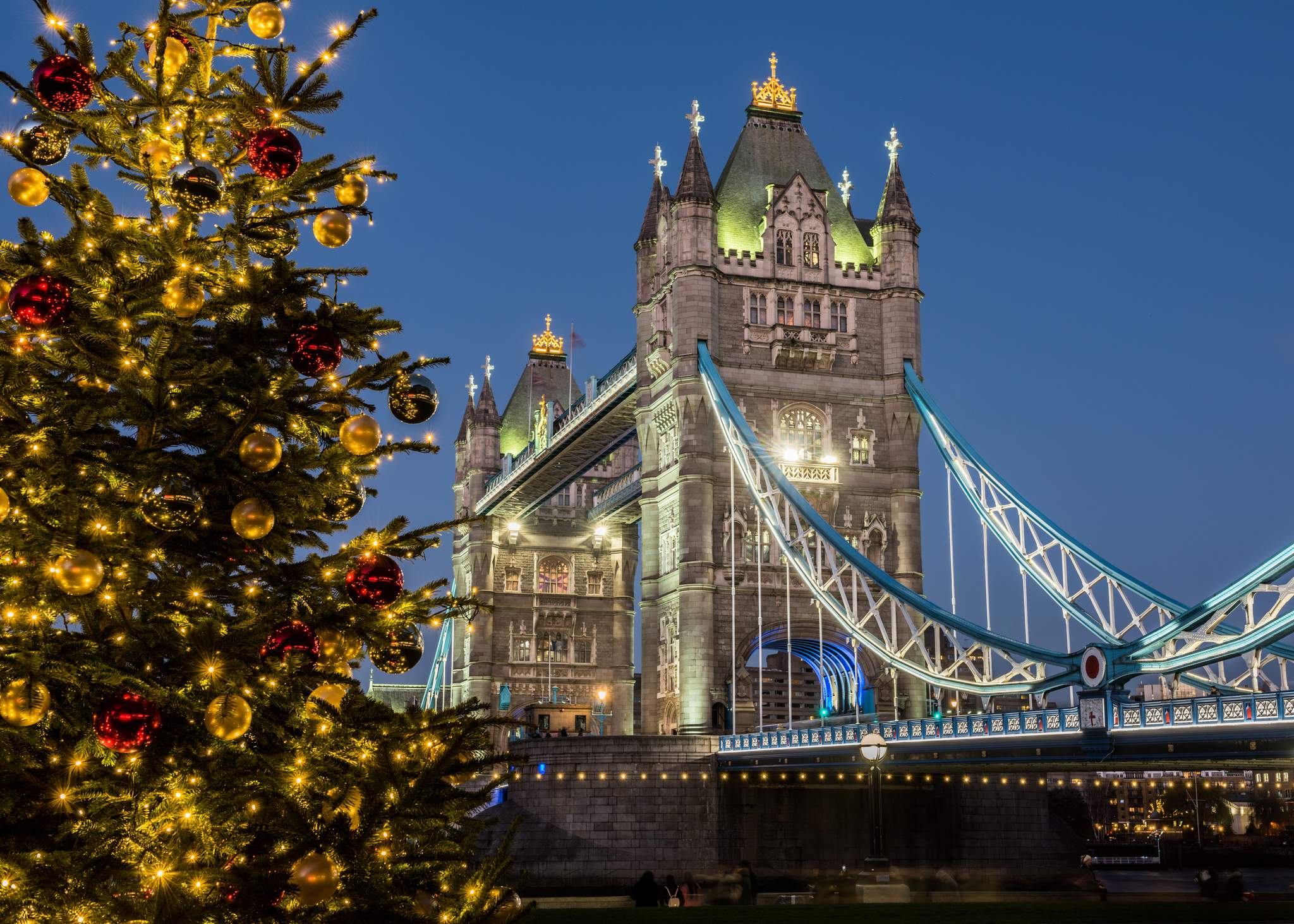 Beleuchtete Tower Bridge in London neben einem festlich geschmückten Weihnachtsbaum am Abend.
