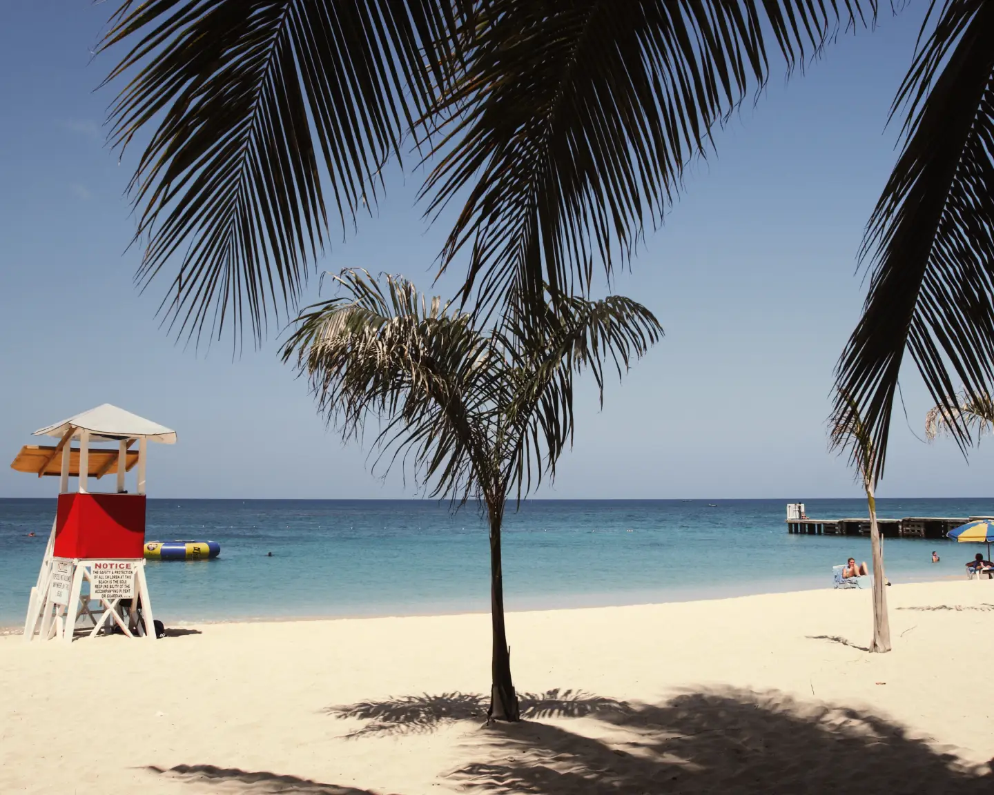 Tropischer Sandstrand mit Palmen, türkisblauem Meer und Rettungsturm an der Karibikküste.