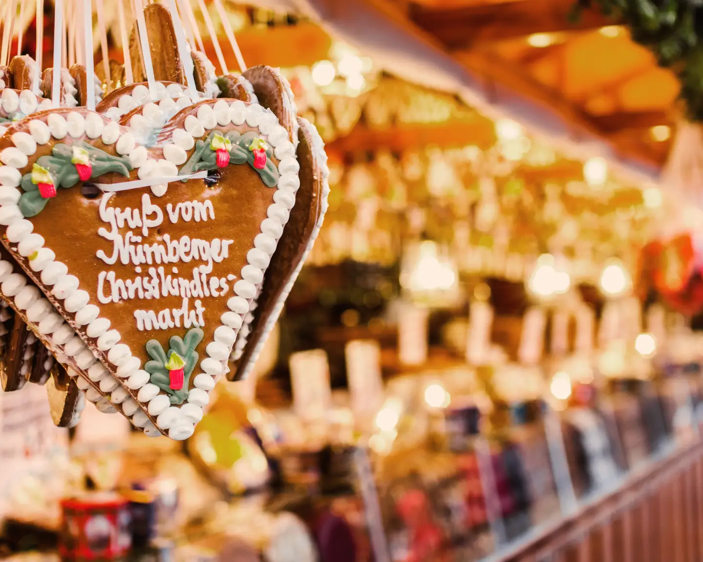 Decorated gingerbread hearts at the Nuremberg Christkindlesmarkt with a festively lit Christmas market stall in the background.