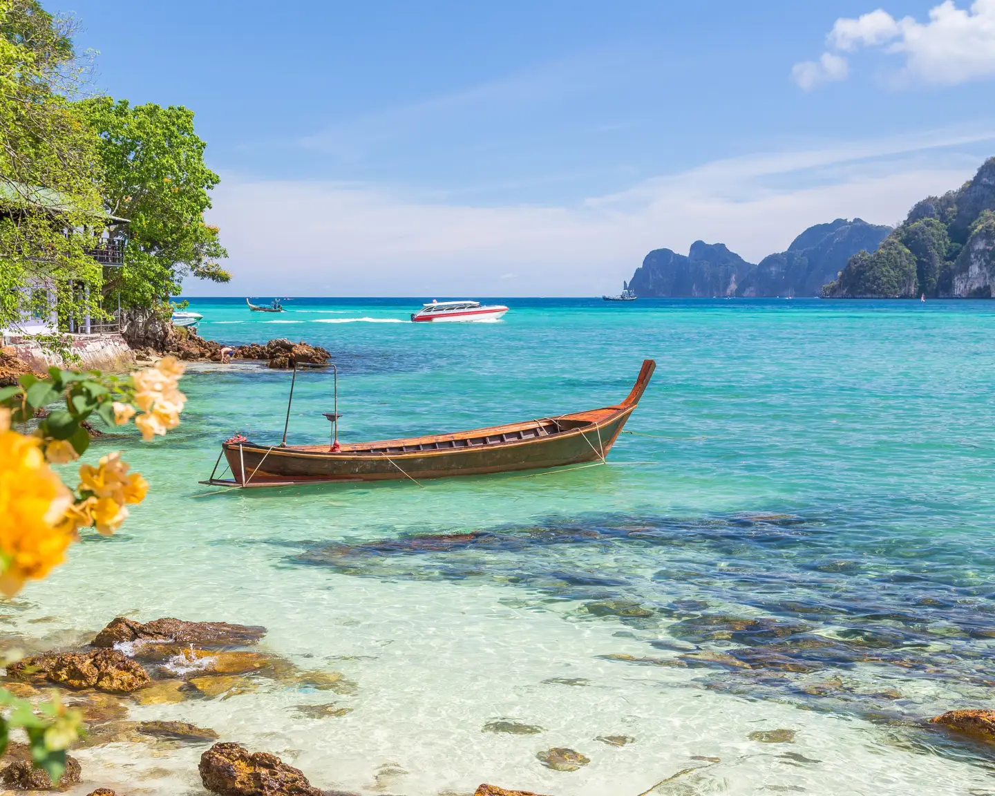 Langboote, die Andamanensee und die Hügel von Ko Phi Phi Don in Südthailand. Klares blaues Wasser und ein wunderschöner Himmel sind zu sehen.