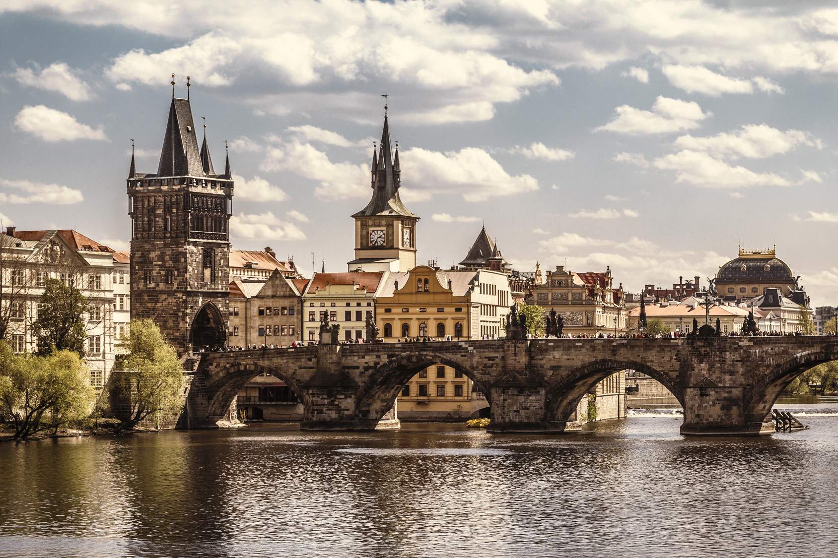 Pont Charles à Prague avec la tour du pont de la vieille ville, la rivière Vltava et l'horizon historique sous un ciel nuageux.