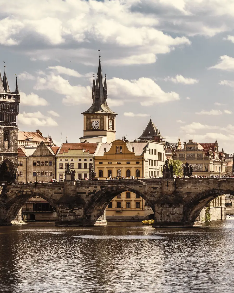Pont Charles à Prague avec la tour du pont de la vieille ville, la rivière Vltava et l'horizon historique sous un ciel nuageux.