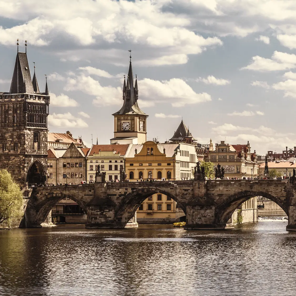Pont Charles à Prague avec la tour du pont de la vieille ville, la rivière Vltava et l'horizon historique sous un ciel nuageux.