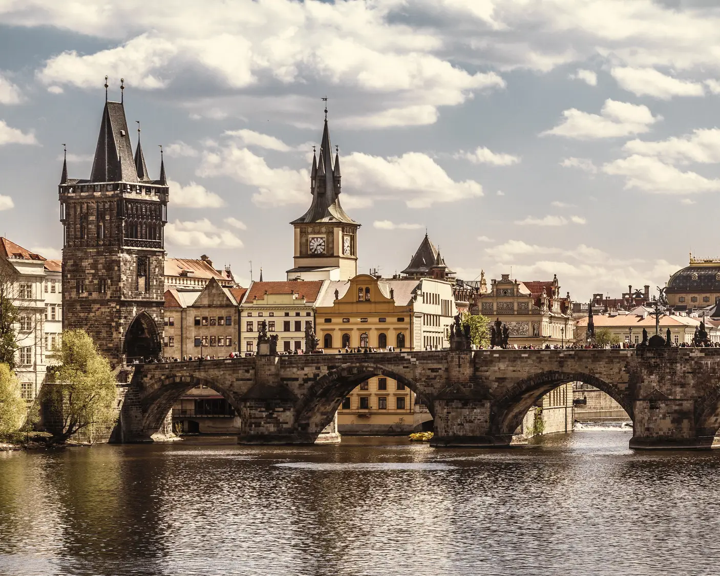 Charles Bridge in Prague, with the Old Town Bridge Tower, the Vltava River and the historic skyline beneath a cloudy sky.