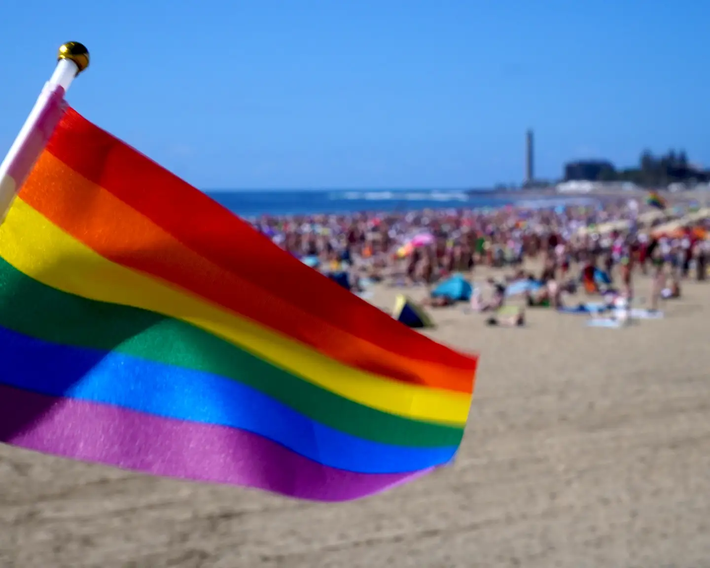 Regenbogenflagge am Strand vor einer Menschenmenge.