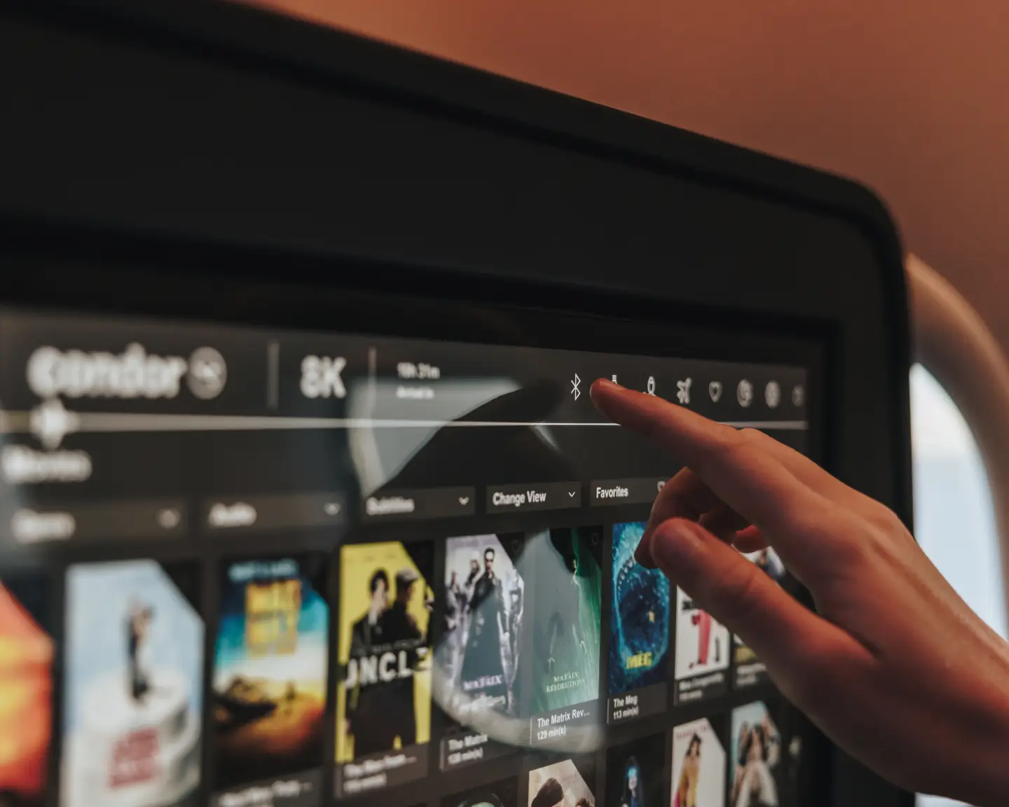 A passenger on bord a plane is browsing the selection of movies available in the inflight entertainment on his personal touch screen