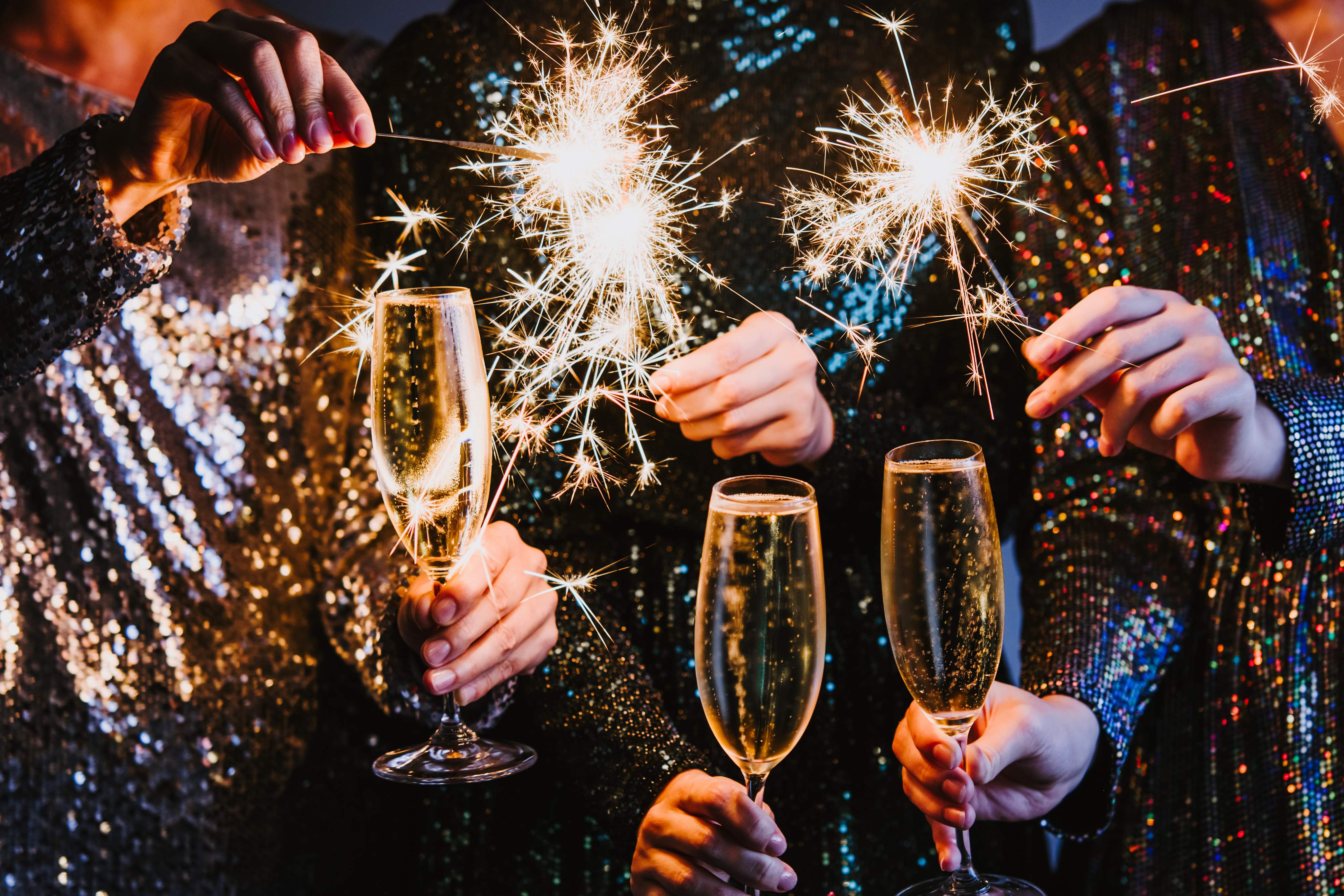 Feiernde Personen stoßen an Silvester mit Sekt an und halten leuchtende Wunderkerzen in den Händen.