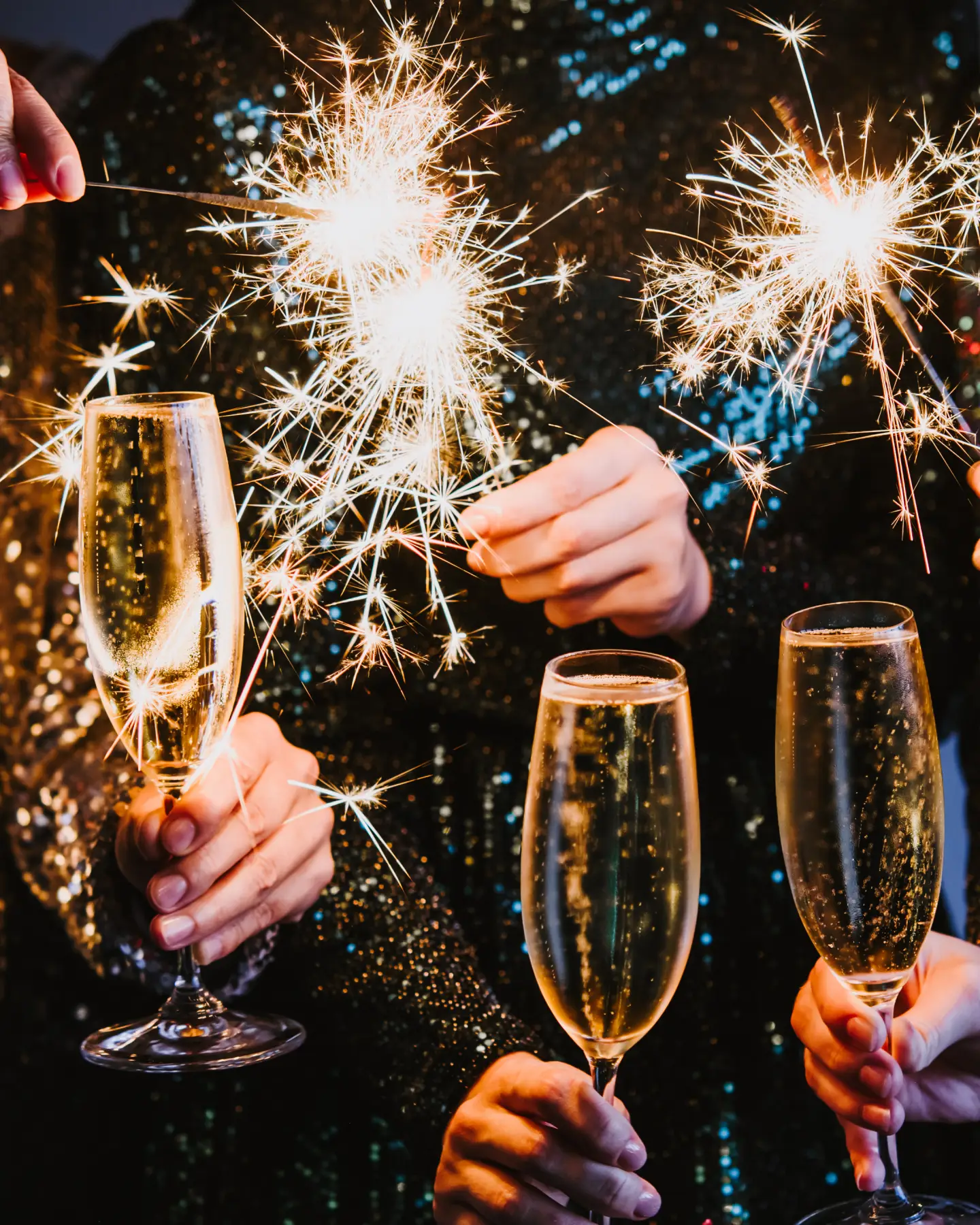 Feiernde Personen stoßen an Silvester mit Sekt an und halten leuchtende Wunderkerzen in den Händen.
