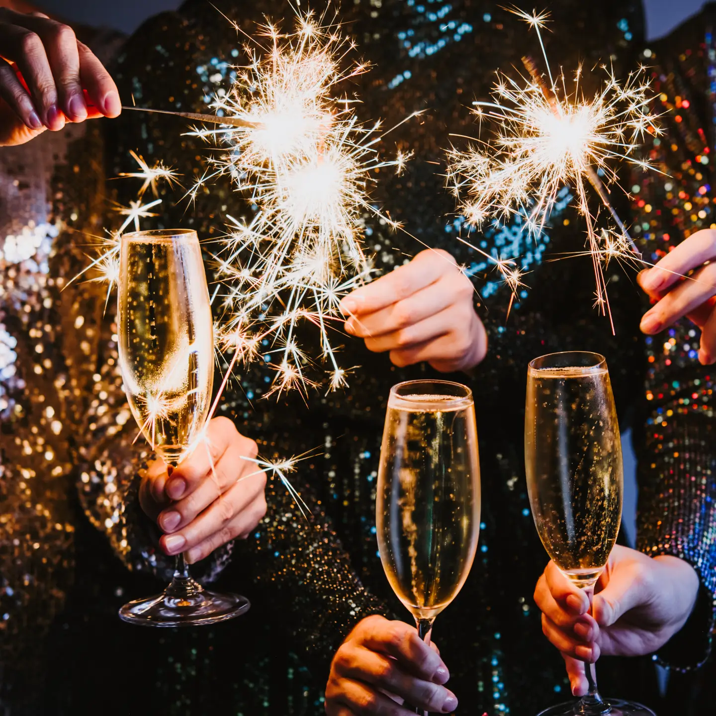 Feiernde Personen stoßen an Silvester mit Sekt an und halten leuchtende Wunderkerzen in den Händen.