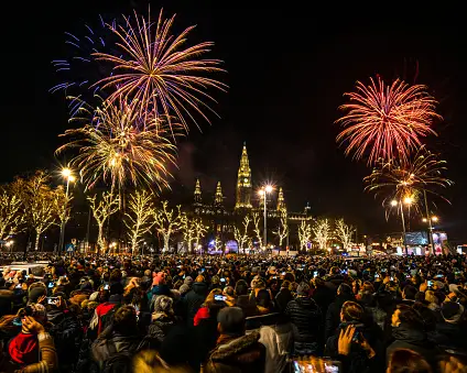 Menschen feiern Silvester auf dem Wiener Rathausplatz bei einem Feuerwerk vor dem beleuchteten Wiener Rathaus.