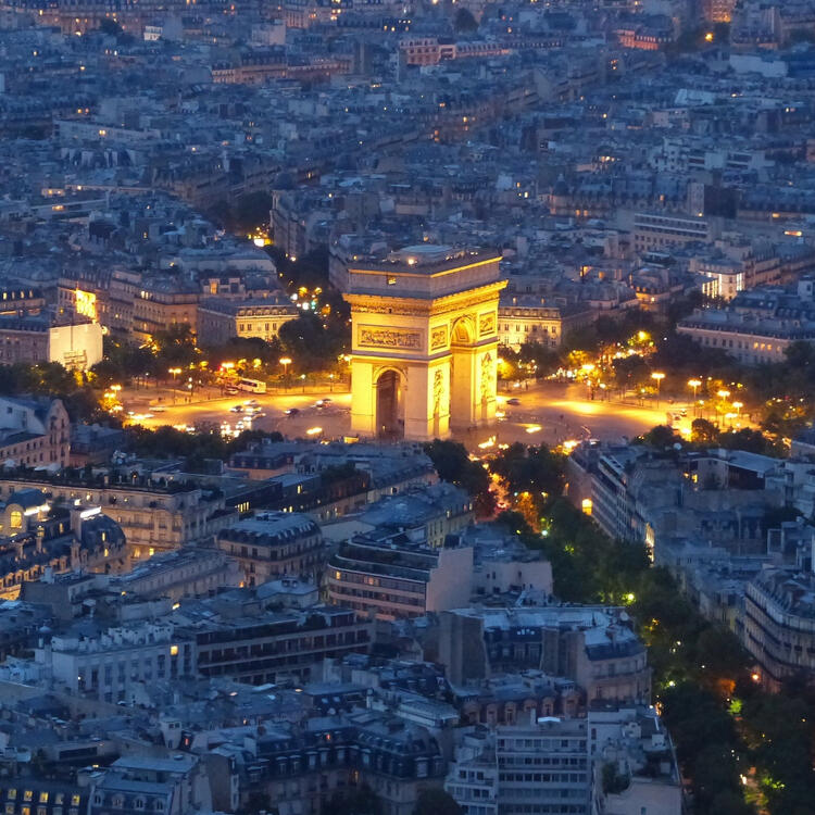 A twilight view of the Arc de Triomphe, warmly lit amidst the sprawling Parisian cityscape.