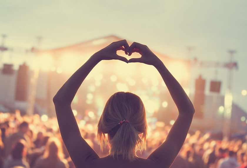 Woman on her back during a concert, with her arms raised and drawing the shape of a heart with her fingers.