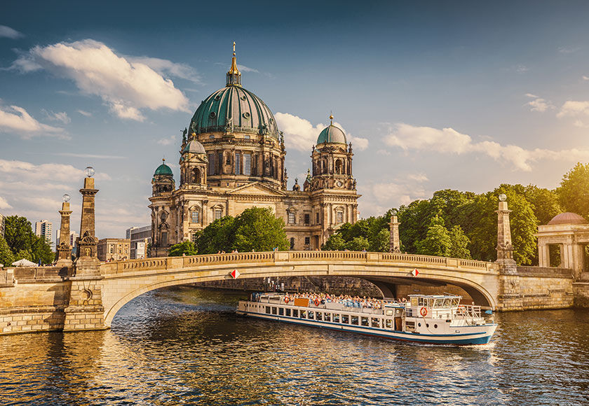 Beautiful view of historic Berlin Cathedral (Berliner Dom) at famous Museum Island with ship passing Friedrichsbrucke bridge on Spree river in golden evening light at sunset in summer, Berlin, Germany