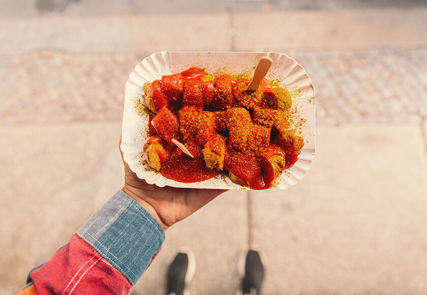 Berlin (BER) Close-up of a person holding a plate of curry-wurst