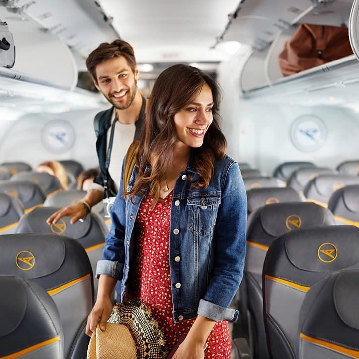 A young couple is walking down the plane isle on a Condor airplane