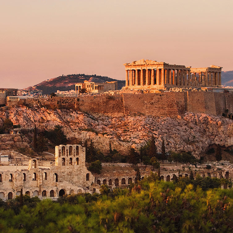 View of the Acropolis in Athens at sunset against an orange sunset sky.