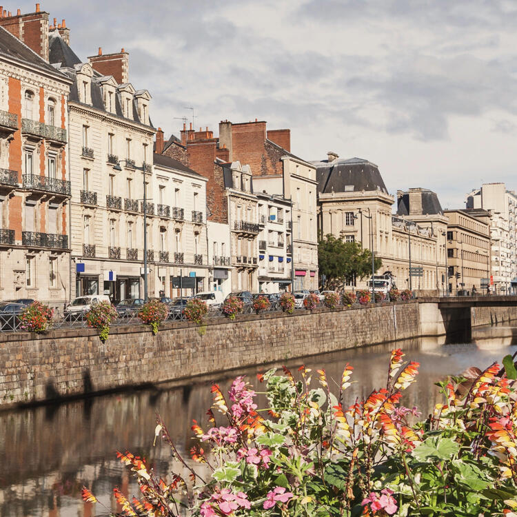 Floral embankments along the river with a view of traditional French architecture in Rennes, France, showcasing historic buildings and a vibrant city atmosphere