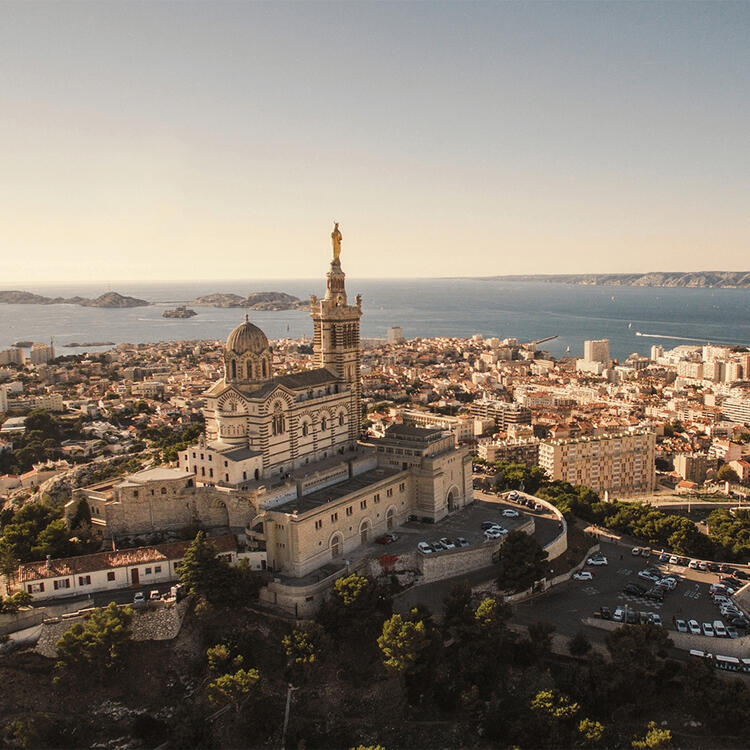 View of the historic Notre-Dame de la Garde basilica overlooking the cityscape of Marseille, France, with the Mediterranean Sea and Frioul archipelago in the background