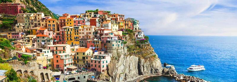View of Manarola, Cinque Terre, in Italy, and the colorful buildings perch on a steep cliffside, overlooking the deep blue sea, capturing the essence of a vibrant coastal town under a soft, expansive sky.