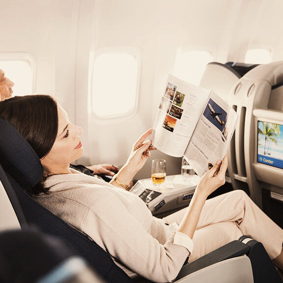 A woman sitting in business class on a plane is relaxing with a magazine and a glass of champagne on her flight