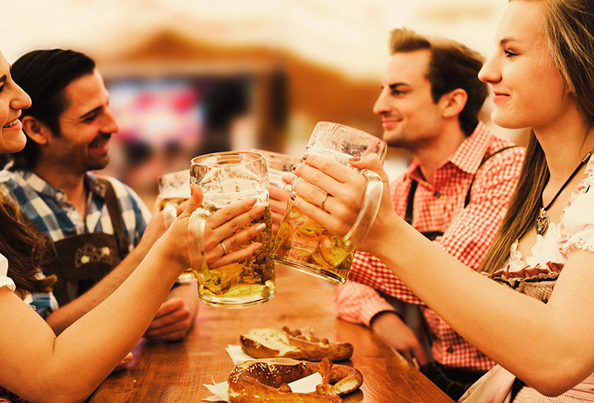 Group of friends, two women and two men, dressed in traditional Bavarian costumes, toasting with Maß beer during the Oktoberfest in Munich.