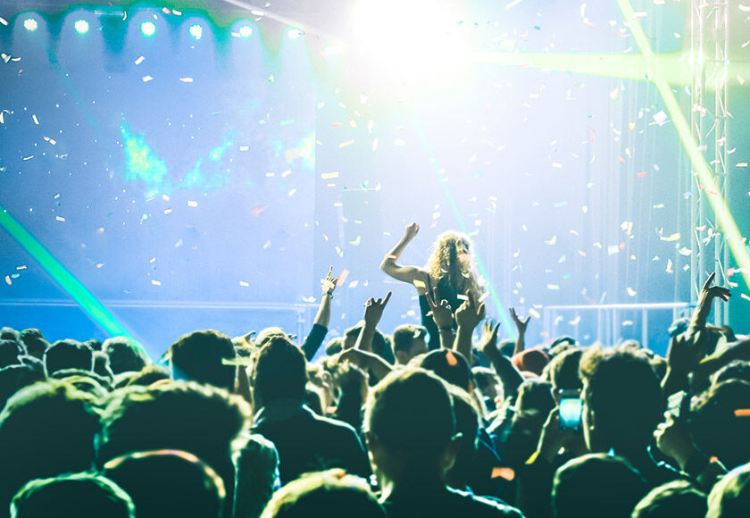 Crowd at a music festival, illuminated by bright stage lights with hands raised in celebration