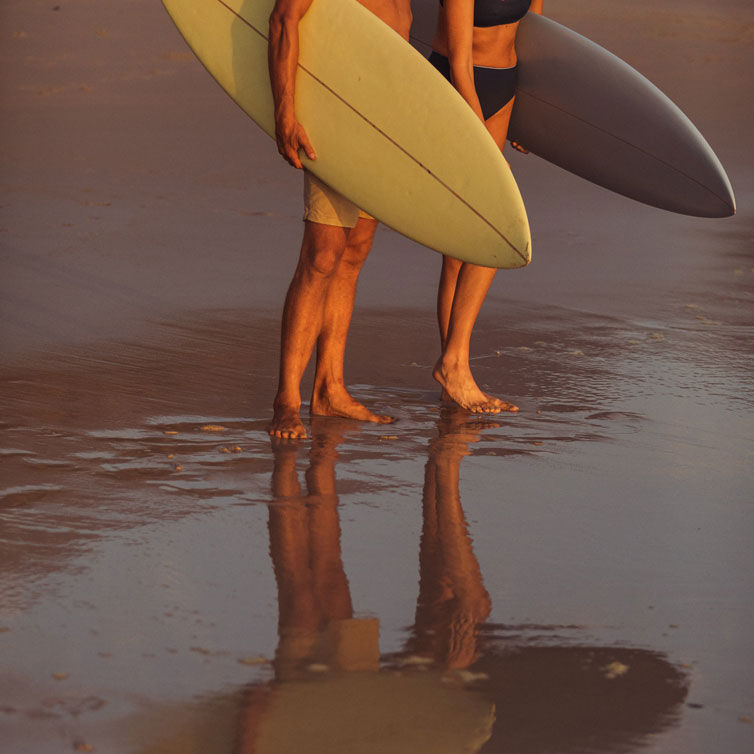 Two surfers stand with their boards on the beach.
