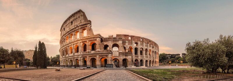  The Colosseum in Rome during golden hour, with its iconic arches illuminated against a serene sky, surrounded by lush greenery.