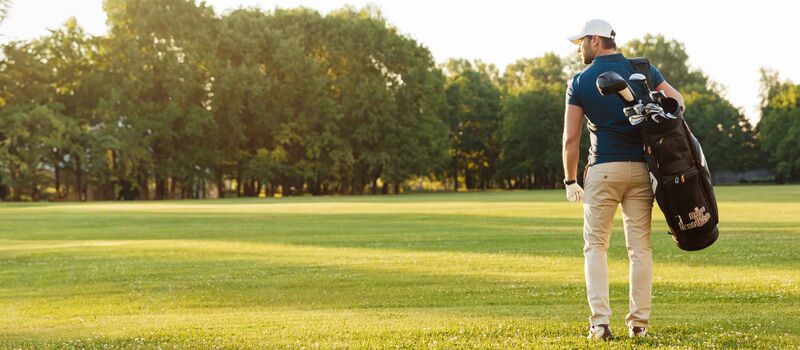 A golfer stands on the green with his golf bag