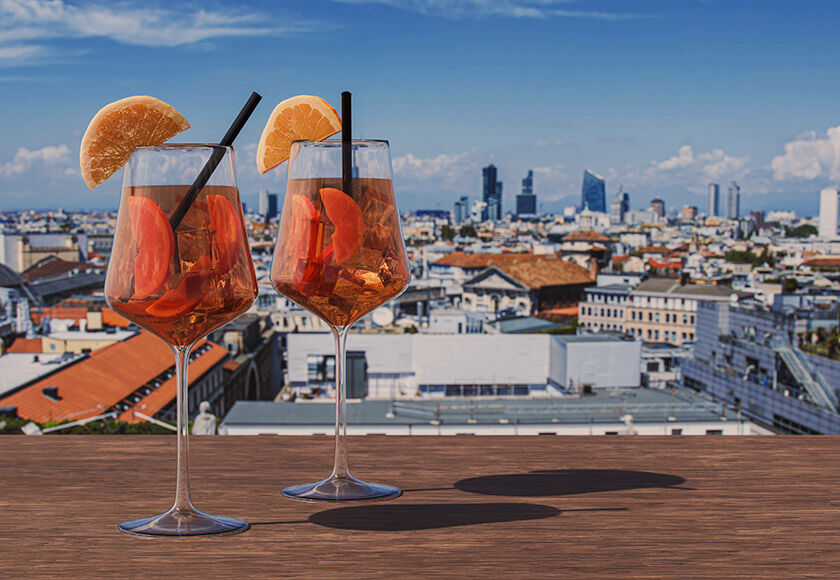 Two Aperol spritz glasses on a Milan rooftop bar with a panoramic view of the town.
