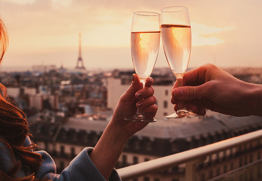 Two people toasting with champagne glasses overlooking the Eiffel Tower at sunset in Paris