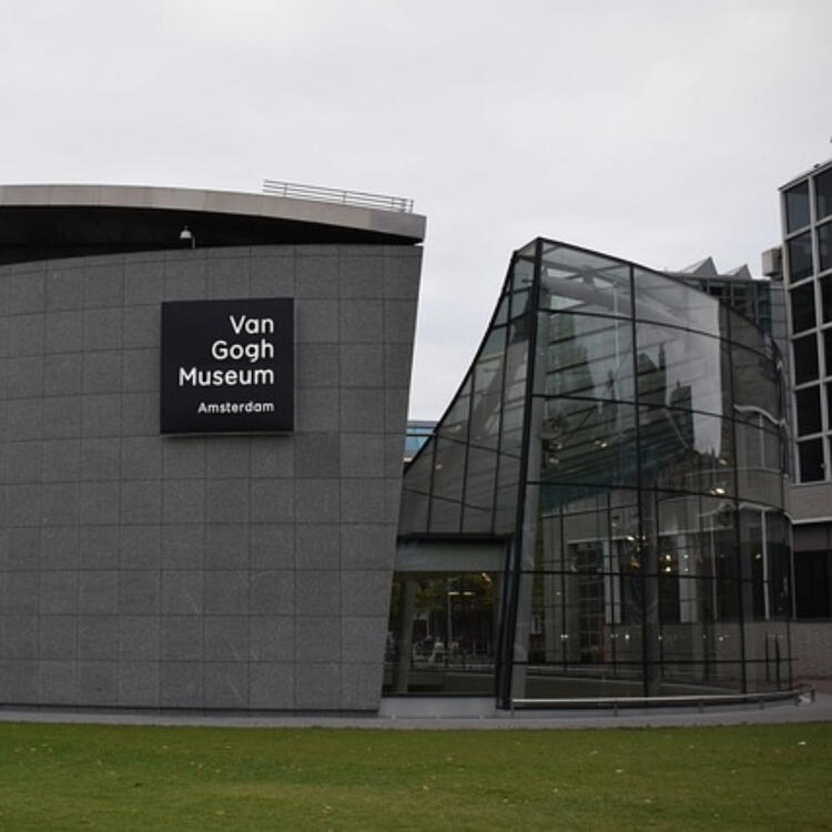 Exterior of the Van Gogh Museum in Amsterdam, featuring a dark grey facade with the museum's name displayed prominently and a modern glass architectural extension adjacent to it