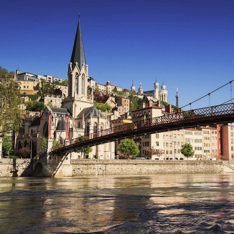Church Saint Georges with metal bridge on the Saone river in Lyon, France, with clear blue skies and the Basilica of Notre-Dame de Fourvière in the distance