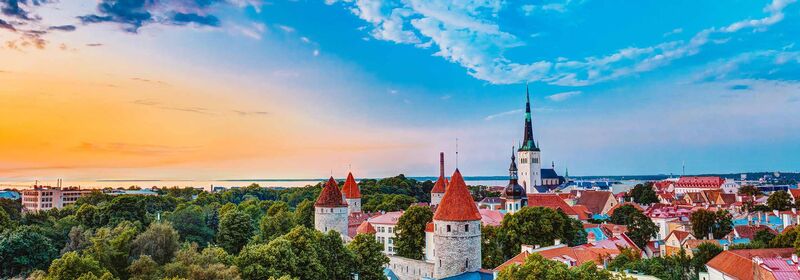 Tallin at sunset, with a prominent church spire rising above red-roofed buildings, set against a gradient sky transitioning from orange to deep blue.