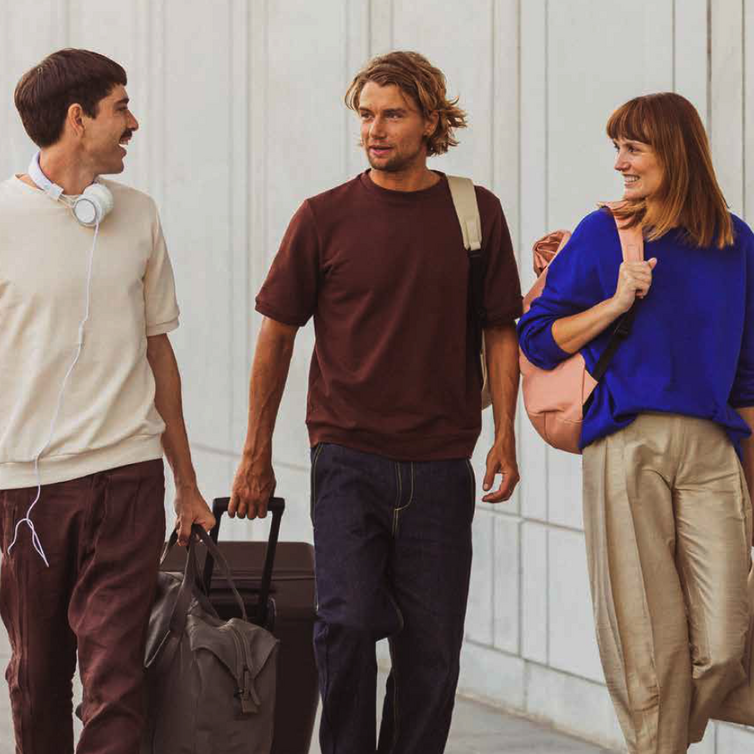 Two men and a woman walking with suitcases and talking at the same time.