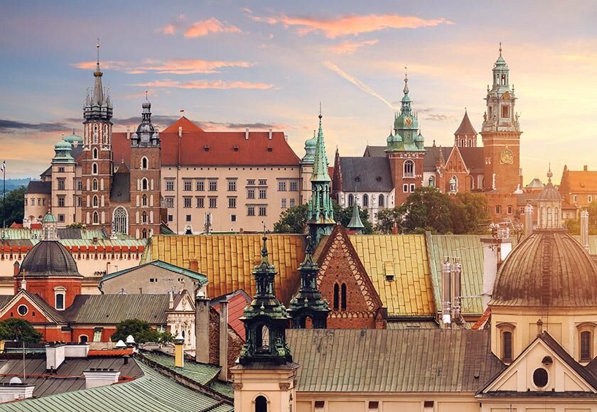 Flights to Krakow (KRK) Historic Riga city skyline at sunset with prominent statues, spires, and riverfront buildings.