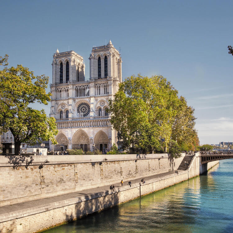Notre-Dame Cathedral beside the Seine River on a sunny day with clear skies.