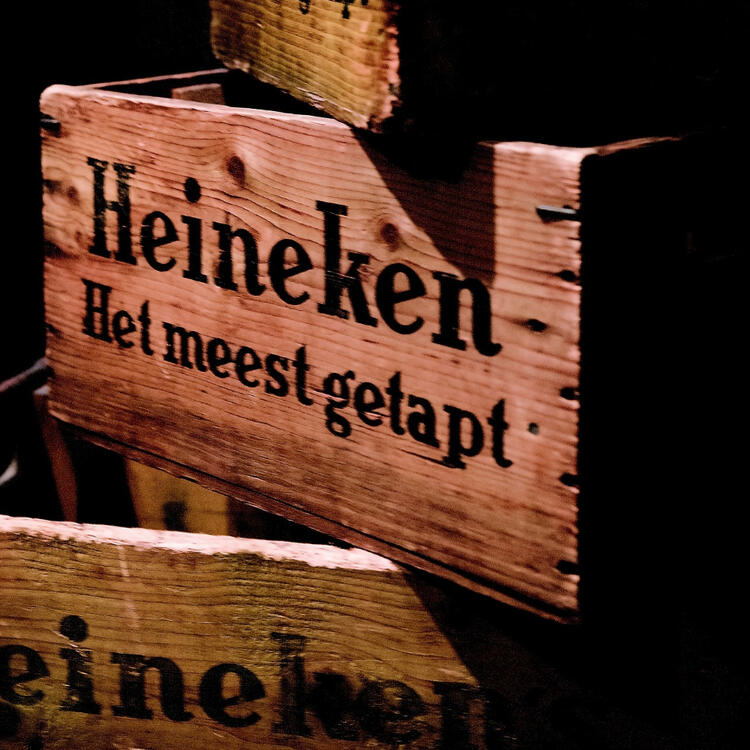 Close-up of rustic wooden crates branded with 'Heineken' and the Dutch text 'Het meest getapt', illuminated in warm lighting.