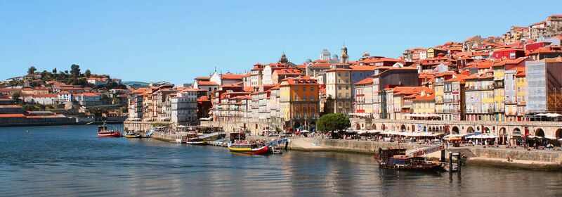 Porto and its picturesque riverside cityscape with colorful buildings, a calm river reflecting the town, and clear blue skies above.