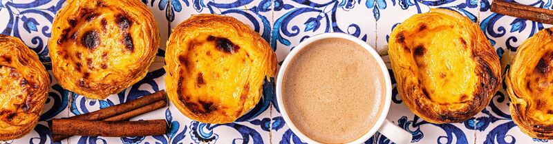 Pastéis de Nata in Lisbon (LIS) Delicious pasteis de nata from Lisbon's Belem neighborhood, accompanied by coffee on a table with traditional white and blue tiles.